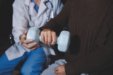 Evde dambıl kullanarak fizyoterapist eğitimi alan yaşlı bir kadın. Terapist, huzurevi egzersizlerinde yaşlı kadına yardım ediyor. Yaşlı bir hasta kollarını uzatmış halterler kullanıyor..