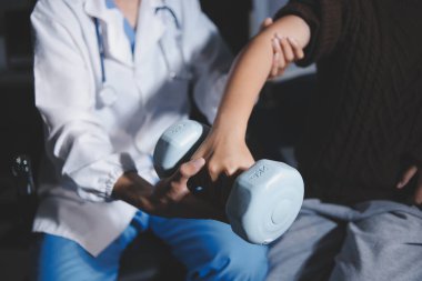 Evde dambıl kullanarak fizyoterapist eğitimi alan yaşlı bir kadın. Terapist, huzurevi egzersizlerinde yaşlı kadına yardım ediyor. Yaşlı bir hasta kollarını uzatmış halterler kullanıyor..