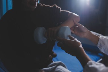 Evde dambıl kullanarak fizyoterapist eğitimi alan yaşlı bir kadın. Terapist, huzurevi egzersizlerinde yaşlı kadına yardım ediyor. Yaşlı bir hasta kollarını uzatmış halterler kullanıyor..