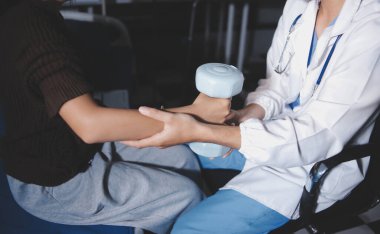 Evde dambıl kullanarak fizyoterapist eğitimi alan yaşlı bir kadın. Terapist, huzurevi egzersizlerinde yaşlı kadına yardım ediyor. Yaşlı bir hasta kollarını uzatmış halterler kullanıyor..