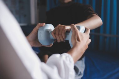 Evde dambıl kullanarak fizyoterapist eğitimi alan yaşlı bir kadın. Terapist, huzurevi egzersizlerinde yaşlı kadına yardım ediyor. Yaşlı bir hasta kollarını uzatmış halterler kullanıyor..