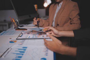 İki iş adamı toplantı odasında proje stratejisi hakkında konuşuyor. İş adamı, mali veri raporu hakkında sohbet ve tavsiyelerde bulunurken, modern işyerindeki iş arkadaşıyla proje planlamasını tartıştı.