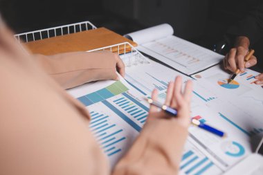 İki iş adamı toplantı odasında proje stratejisi hakkında konuşuyor. İş adamı, mali veri raporu hakkında sohbet ve tavsiyelerde bulunurken, modern işyerindeki iş arkadaşıyla proje planlamasını tartıştı.