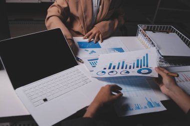 İki iş adamı toplantı odasında proje stratejisi hakkında konuşuyor. İş adamı, mali veri raporu hakkında sohbet ve tavsiyelerde bulunurken, modern işyerindeki iş arkadaşıyla proje planlamasını tartıştı.