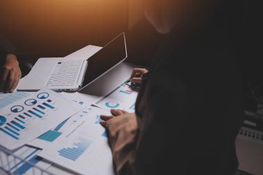 İki iş adamı toplantı odasında proje stratejisi hakkında konuşuyor. İş adamı, mali veri raporu hakkında sohbet ve tavsiyelerde bulunurken, modern işyerindeki iş arkadaşıyla proje planlamasını tartıştı.