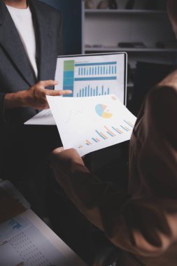 İki iş adamı toplantı odasında proje stratejisi hakkında konuşuyor. İş adamı, mali veri raporu hakkında sohbet ve tavsiyelerde bulunurken, modern işyerindeki iş arkadaşıyla proje planlamasını tartıştı.