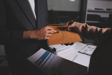 İki iş adamı toplantı odasında proje stratejisi hakkında konuşuyor. İş adamı, mali veri raporu hakkında sohbet ve tavsiyelerde bulunurken, modern işyerindeki iş arkadaşıyla proje planlamasını tartıştı.