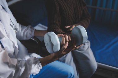 Evde dambıl kullanarak fizyoterapist eğitimi alan yaşlı bir kadın. Terapist, huzurevi egzersizlerinde yaşlı kadına yardım ediyor. Yaşlı bir hasta kollarını uzatmış halterler kullanıyor..