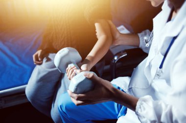 Evde dambıl kullanarak fizyoterapist eğitimi alan yaşlı bir kadın. Terapist, huzurevi egzersizlerinde yaşlı kadına yardım ediyor. Yaşlı bir hasta kollarını uzatmış halterler kullanıyor..