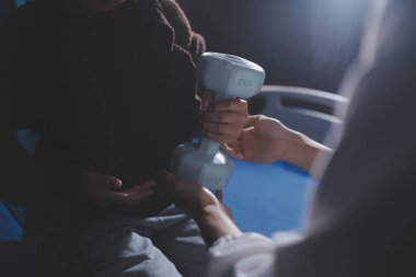 Evde dambıl kullanarak fizyoterapist eğitimi alan yaşlı bir kadın. Terapist, huzurevi egzersizlerinde yaşlı kadına yardım ediyor. Yaşlı bir hasta kollarını uzatmış halterler kullanıyor..