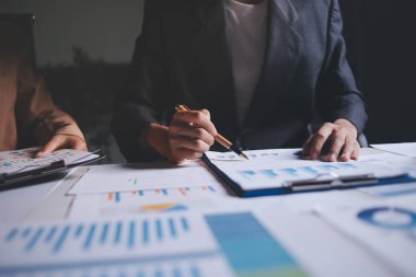 İki iş adamı toplantı odasında proje stratejisi hakkında konuşuyor. İş adamı, mali veri raporu hakkında sohbet ve tavsiyelerde bulunurken, modern işyerindeki iş arkadaşıyla proje planlamasını tartıştı.