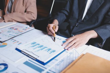 İki iş adamı toplantı odasında proje stratejisi hakkında konuşuyor. İş adamı, mali veri raporu hakkında sohbet ve tavsiyelerde bulunurken, modern işyerindeki iş arkadaşıyla proje planlamasını tartıştı.