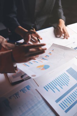 İki iş adamı toplantı odasında proje stratejisi hakkında konuşuyor. İş adamı, mali veri raporu hakkında sohbet ve tavsiyelerde bulunurken, modern işyerindeki iş arkadaşıyla proje planlamasını tartıştı.