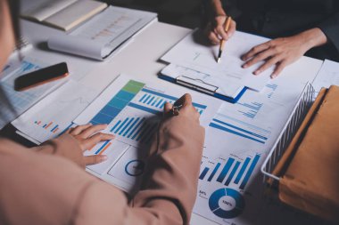 İki iş adamı toplantı odasında proje stratejisi hakkında konuşuyor. İş adamı, mali veri raporu hakkında sohbet ve tavsiyelerde bulunurken, modern işyerindeki iş arkadaşıyla proje planlamasını tartıştı.