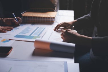 İki iş adamı toplantı odasında proje stratejisi hakkında konuşuyor. İş adamı, mali veri raporu hakkında sohbet ve tavsiyelerde bulunurken, modern işyerindeki iş arkadaşıyla proje planlamasını tartıştı.