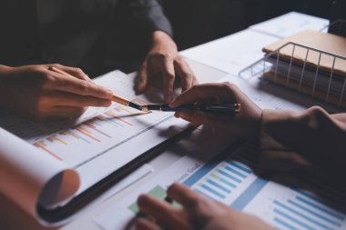 İki iş adamı toplantı odasında proje stratejisi hakkında konuşuyor. İş adamı, mali veri raporu hakkında sohbet ve tavsiyelerde bulunurken, modern işyerindeki iş arkadaşıyla proje planlamasını tartıştı.