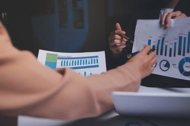 İki iş adamı toplantı odasında proje stratejisi hakkında konuşuyor. İş adamı, mali veri raporu hakkında sohbet ve tavsiyelerde bulunurken, modern işyerindeki iş arkadaşıyla proje planlamasını tartıştı.