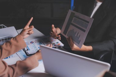 İki iş adamı toplantı odasında proje stratejisi hakkında konuşuyor. İş adamı, mali veri raporu hakkında sohbet ve tavsiyelerde bulunurken, modern işyerindeki iş arkadaşıyla proje planlamasını tartıştı.