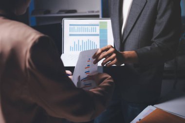 İki iş adamı toplantı odasında proje stratejisi hakkında konuşuyor. İş adamı, mali veri raporu hakkında sohbet ve tavsiyelerde bulunurken, modern işyerindeki iş arkadaşıyla proje planlamasını tartıştı.