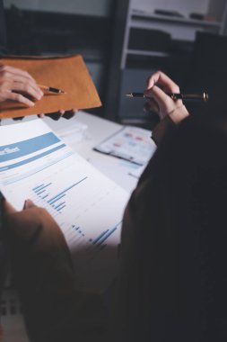 İki iş adamı toplantı odasında proje stratejisi hakkında konuşuyor. İş adamı, mali veri raporu hakkında sohbet ve tavsiyelerde bulunurken, modern işyerindeki iş arkadaşıyla proje planlamasını tartıştı.