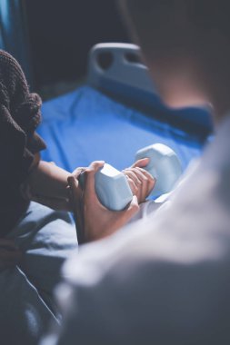 Evde dambıl kullanarak fizyoterapist eğitimi alan yaşlı bir kadın. Terapist, huzurevi egzersizlerinde yaşlı kadına yardım ediyor. Yaşlı bir hasta kollarını uzatmış halterler kullanıyor..