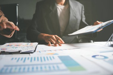 İki iş adamı toplantı odasında proje stratejisi hakkında konuşuyor. İş adamı, mali veri raporu hakkında sohbet ve tavsiyelerde bulunurken, modern işyerindeki iş arkadaşıyla proje planlamasını tartıştı.