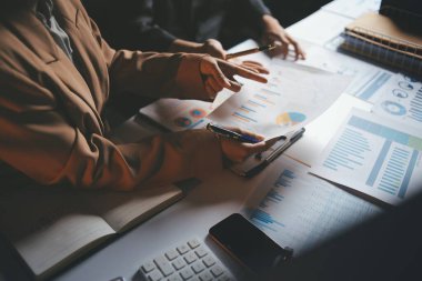 İki iş adamı toplantı odasında proje stratejisi hakkında konuşuyor. İş adamı, mali veri raporu hakkında sohbet ve tavsiyelerde bulunurken, modern işyerindeki iş arkadaşıyla proje planlamasını tartıştı.