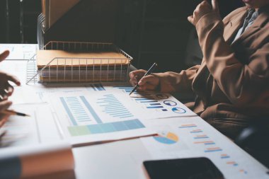 İki iş adamı toplantı odasında proje stratejisi hakkında konuşuyor. İş adamı, mali veri raporu hakkında sohbet ve tavsiyelerde bulunurken, modern işyerindeki iş arkadaşıyla proje planlamasını tartıştı.