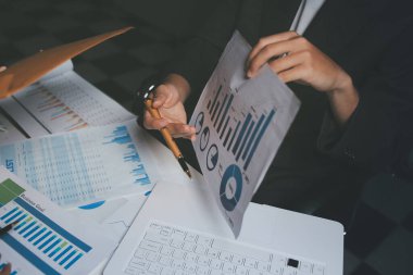 İki iş adamı toplantı odasında proje stratejisi hakkında konuşuyor. İş adamı, mali veri raporu hakkında sohbet ve tavsiyelerde bulunurken, modern işyerindeki iş arkadaşıyla proje planlamasını tartıştı.