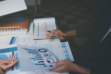 İki iş adamı toplantı odasında proje stratejisi hakkında konuşuyor. İş adamı, mali veri raporu hakkında sohbet ve tavsiyelerde bulunurken, modern işyerindeki iş arkadaşıyla proje planlamasını tartıştı.