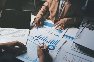 İki iş adamı toplantı odasında proje stratejisi hakkında konuşuyor. İş adamı, mali veri raporu hakkında sohbet ve tavsiyelerde bulunurken, modern işyerindeki iş arkadaşıyla proje planlamasını tartıştı.