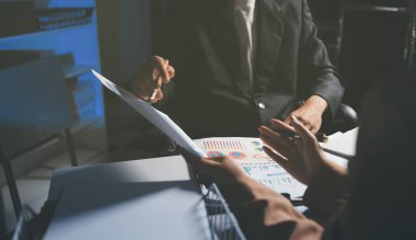 İki iş adamı toplantı odasında proje stratejisi hakkında konuşuyor. İş adamı, mali veri raporu hakkında sohbet ve tavsiyelerde bulunurken, modern işyerindeki iş arkadaşıyla proje planlamasını tartıştı.