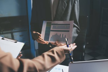 İki iş adamı toplantı odasında proje stratejisi hakkında konuşuyor. İş adamı, mali veri raporu hakkında sohbet ve tavsiyelerde bulunurken, modern işyerindeki iş arkadaşıyla proje planlamasını tartıştı.