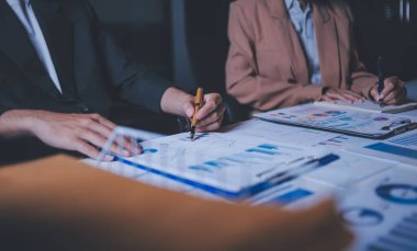 İki iş adamı toplantı odasında proje stratejisi hakkında konuşuyor. İş adamı, mali veri raporu hakkında sohbet ve tavsiyelerde bulunurken, modern işyerindeki iş arkadaşıyla proje planlamasını tartıştı.