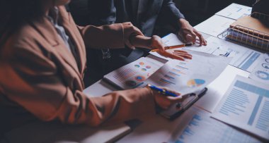 İki iş adamı toplantı odasında proje stratejisi hakkında konuşuyor. İş adamı, mali veri raporu hakkında sohbet ve tavsiyelerde bulunurken, modern işyerindeki iş arkadaşıyla proje planlamasını tartıştı.