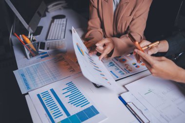 İki iş adamı toplantı odasında proje stratejisi hakkında konuşuyor. İş adamı, mali veri raporu hakkında sohbet ve tavsiyelerde bulunurken, modern işyerindeki iş arkadaşıyla proje planlamasını tartıştı.