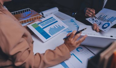 İki iş adamı toplantı odasında proje stratejisi hakkında konuşuyor. İş adamı, mali veri raporu hakkında sohbet ve tavsiyelerde bulunurken, modern işyerindeki iş arkadaşıyla proje planlamasını tartıştı.