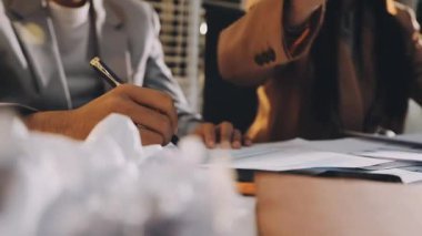 Karmaşık ofis masasında hesap makinesiyle basılı mali raporları inceleyen muhasebeci, denetim ve kurumsal finans işleri için yumuşak pencere ışığı altında yapışkan notlar tutuyor.