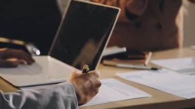 Karmaşık ofis masasında hesap makinesiyle basılı mali raporları inceleyen muhasebeci, denetim ve kurumsal finans işleri için yumuşak pencere ışığı altında yapışkan notlar tutuyor.