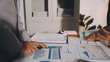 Karmaşık ofis masasında hesap makinesiyle basılı mali raporları inceleyen muhasebeci, denetim ve kurumsal finans işleri için yumuşak pencere ışığı altında yapışkan notlar tutuyor.