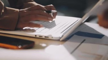 Karmaşık ofis masasında hesap makinesiyle basılı mali raporları inceleyen muhasebeci, denetim ve kurumsal finans işleri için yumuşak pencere ışığı altında yapışkan notlar tutuyor.