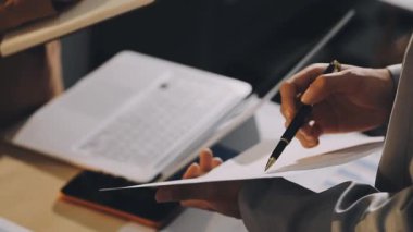 Karmaşık ofis masasında hesap makinesiyle basılı mali raporları inceleyen muhasebeci, denetim ve kurumsal finans işleri için yumuşak pencere ışığı altında yapışkan notlar tutuyor.