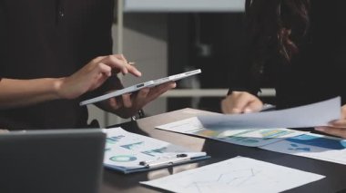 Genç Asyalı iş kadını birlikte çalışıyor ve ofisteki dizüstü bilgisayardaki finansal verileri iş adamlarıyla tartışıyor..