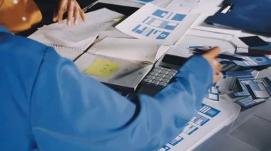 Ofiste bilgisayar ve tabletle masada otururken cep telefonu kullanan genç Asyalı kadın tasarımcı..