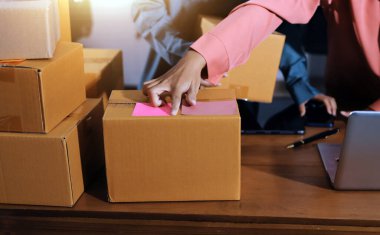 Girişim KOBİ küçük işletme girişimcisi önlük giyen Asyalı kadın dizüstü bilgisayar ve kutu kullanarak çevrimiçi müşterilere, çevrimiçi sme iş fikirlerine satış hazırlamak için siparişleri alır ve gözden geçirir.