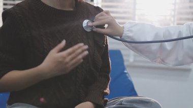 Yaşlı hastaların hayati organlarını incelemek için steteskop kullanan sevimli genç Latin doktor. Çekici İspanyol doktor, beyaz yaşlı bir kadının kalbini ve ciğerlerini kontrol etmek için tıbbi bir alet kullanıyor.