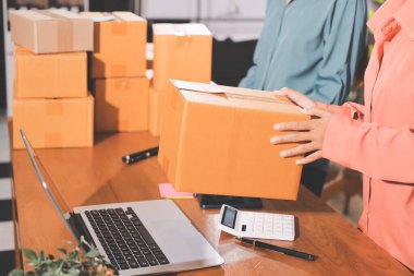 Girişim KOBİ küçük işletme girişimcisi önlük giyen Asyalı kadın dizüstü bilgisayar ve kutu kullanarak çevrimiçi müşterilere, çevrimiçi sme iş fikirlerine satış hazırlamak için siparişleri alır ve gözden geçirir.