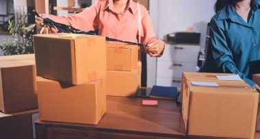 Girişim KOBİ küçük işletme girişimcisi önlük giyen Asyalı kadın dizüstü bilgisayar ve kutu kullanarak çevrimiçi müşterilere, çevrimiçi sme iş fikirlerine satış hazırlamak için siparişleri alır ve gözden geçirir.