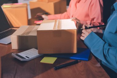 Girişim KOBİ küçük işletme girişimcisi önlük giyen Asyalı kadın dizüstü bilgisayar ve kutu kullanarak çevrimiçi müşterilere, çevrimiçi sme iş fikirlerine satış hazırlamak için siparişleri alır ve gözden geçirir.