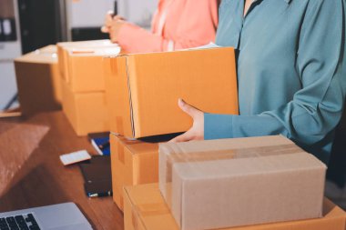 Girişim KOBİ küçük işletme girişimcisi önlük giyen Asyalı kadın dizüstü bilgisayar ve kutu kullanarak çevrimiçi müşterilere, çevrimiçi sme iş fikirlerine satış hazırlamak için siparişleri alır ve gözden geçirir.